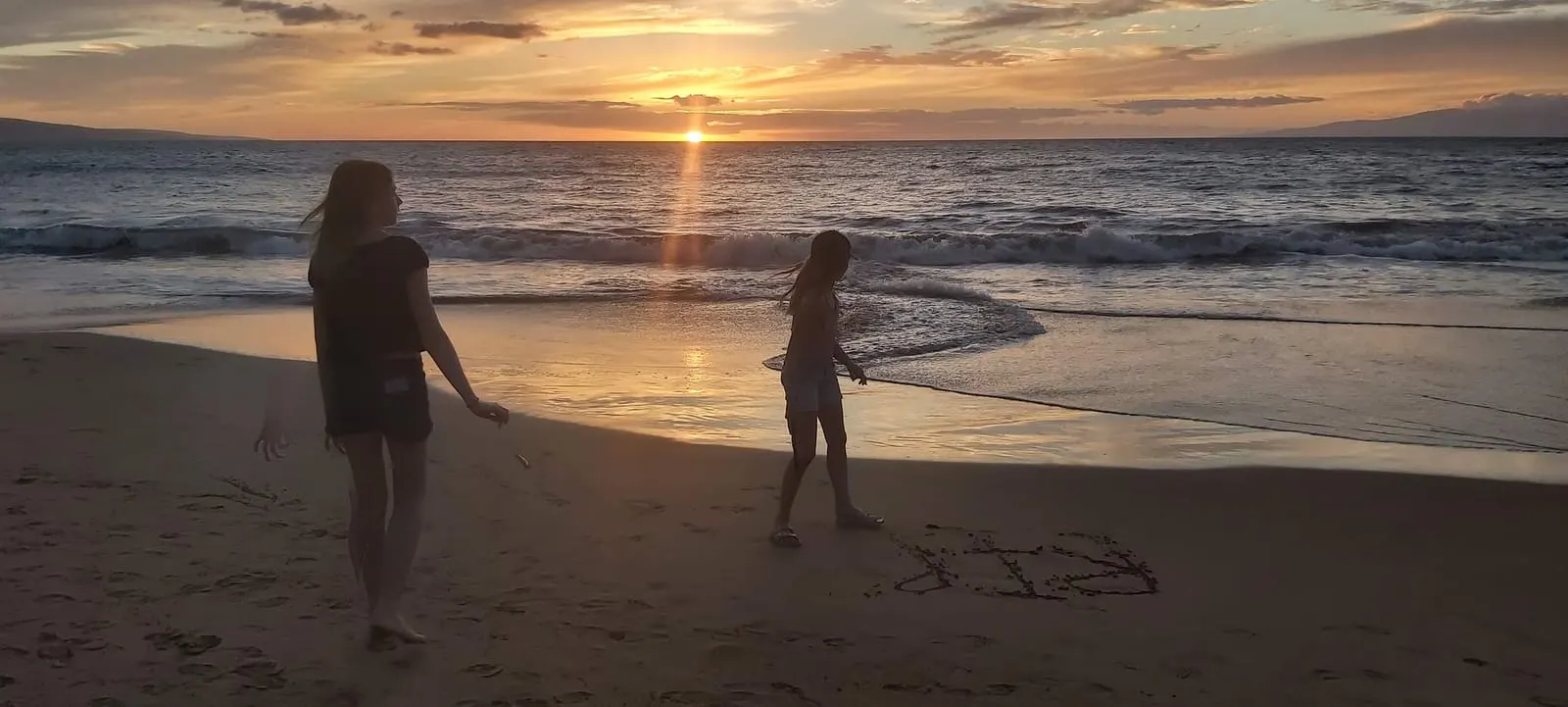 Beachgoers watching a Maui ocean sunset