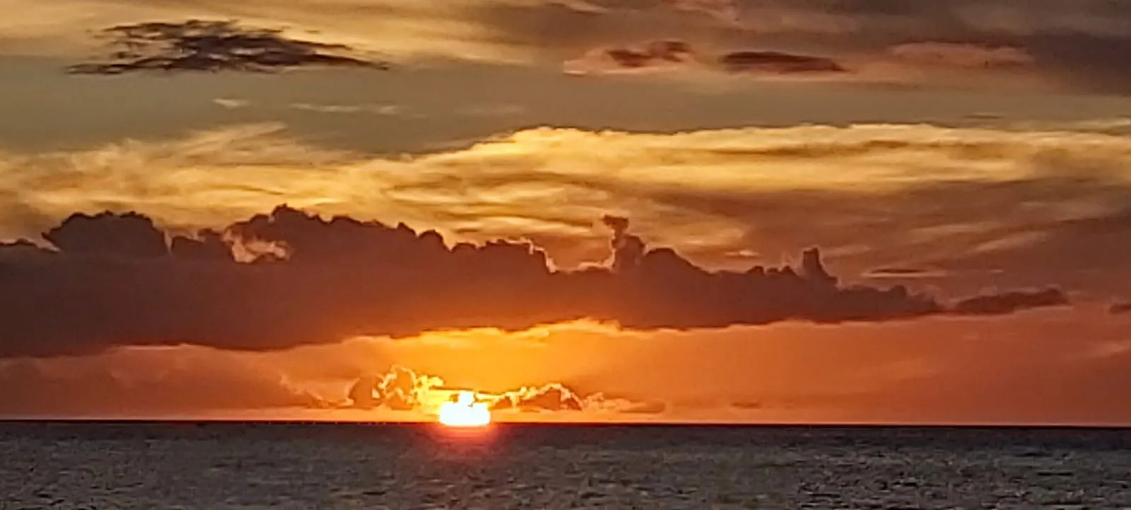 Orange sun setting beneath dark ocean clouds