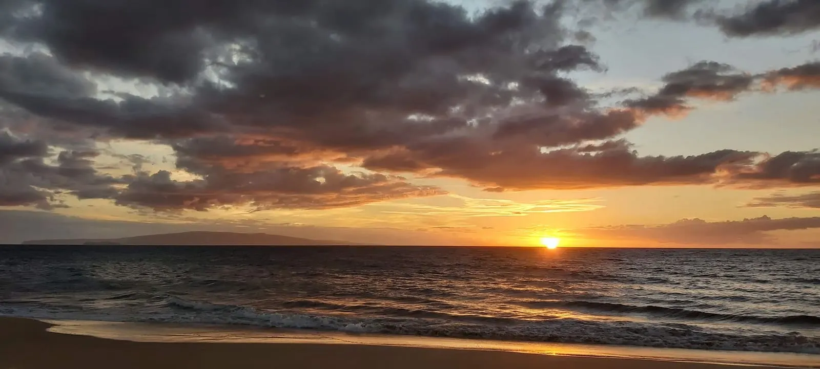 Sunset reflecting on waves beneath a cloudy sky