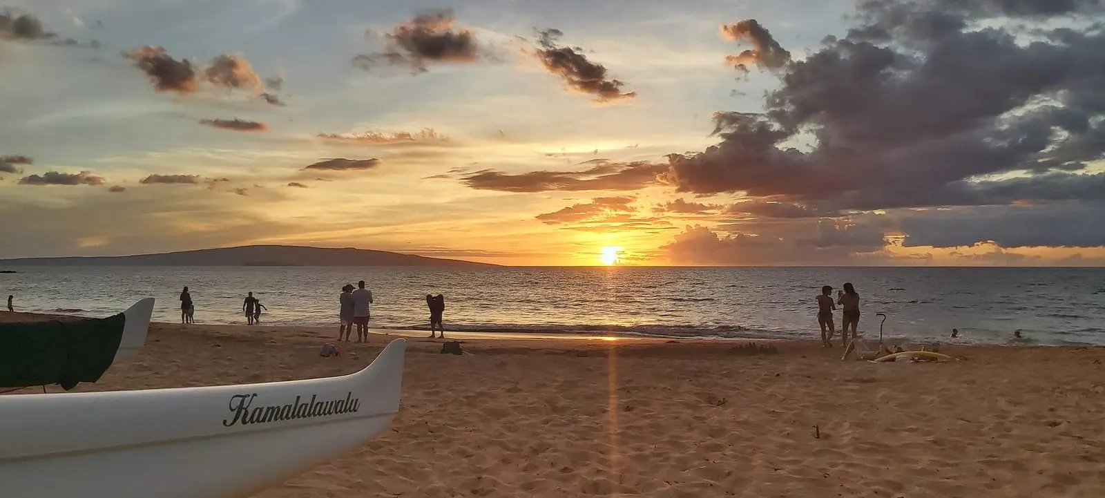 Canoe on the beach as visitors watch the sunset