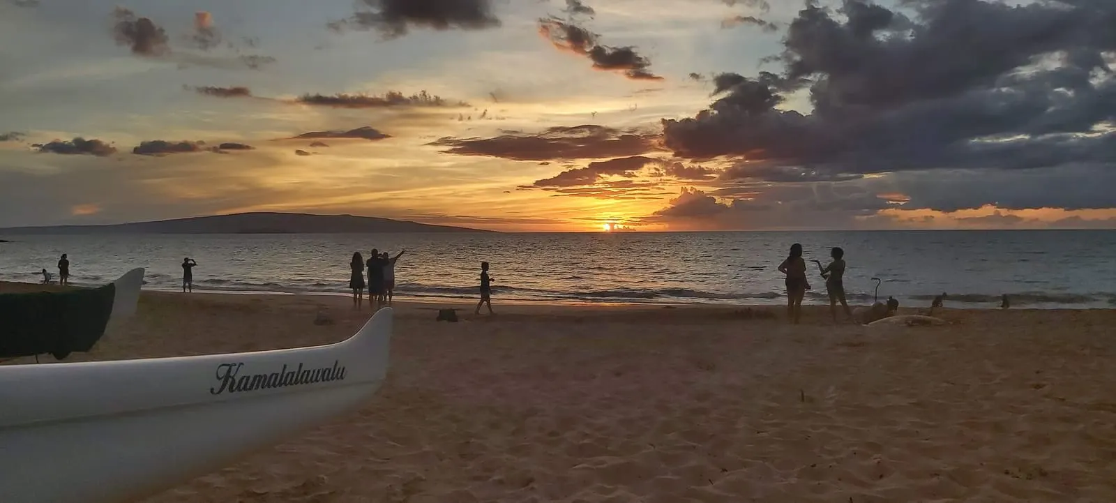 Beachgoers along the shoreline at sunset