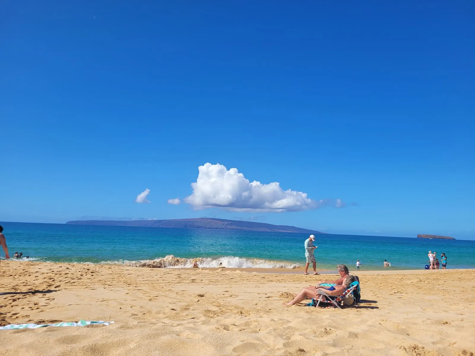 Sunny sandy beach with blue water and distant mountains