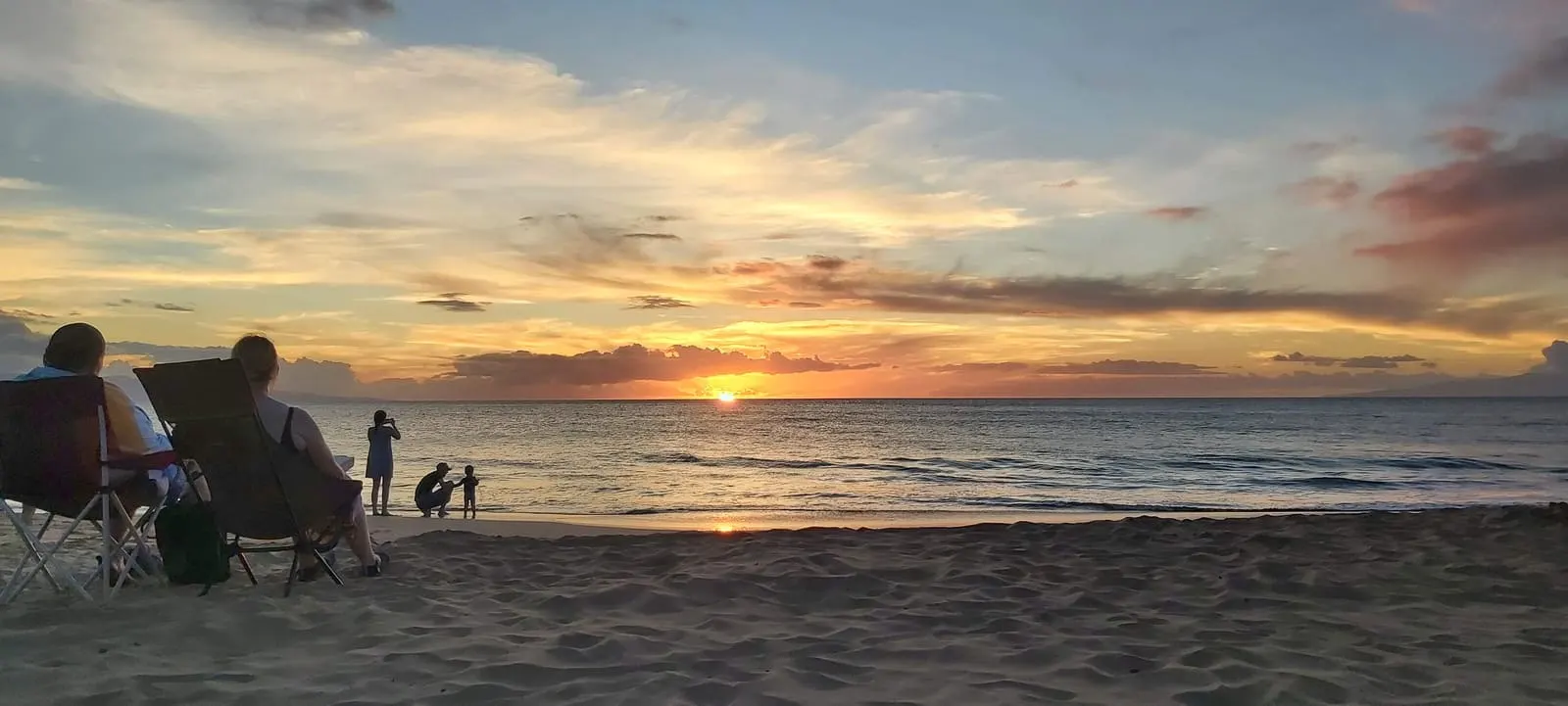 Visitors seated beside the shoreline at sunset